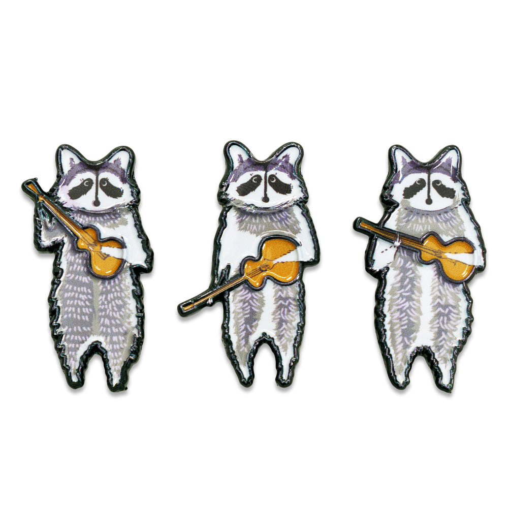 Three raccoon band enamel pins with white fur, gold instrument, yellow accents